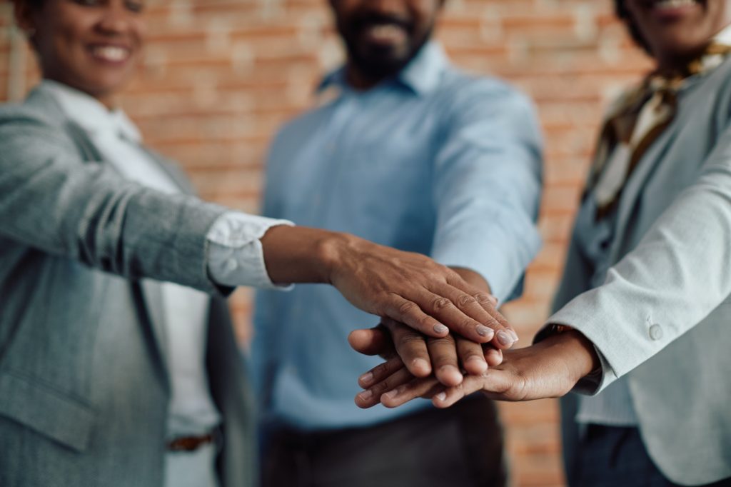 Close-up of black business team gathering hands in unity in the office.